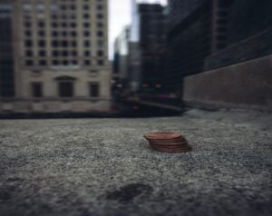 Stack of pennies on a concrete sidewalk with tall buildings blurred in the background.